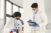 Dois cientistas trabalham com um microscópio e uma prancheta em um laboratório.