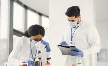Dois cientistas trabalham com um microscópio e uma prancheta em um laboratório.