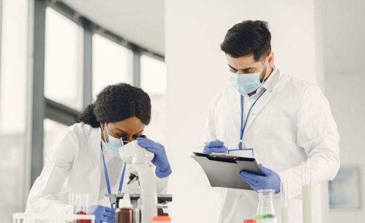 Dois cientistas trabalham com um microscópio e uma prancheta em um laboratório.