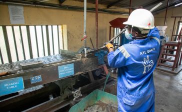 Trabalhador usando uniforme azul opera uma mesa vibratória para processamento de minério em uma unidade industrial.