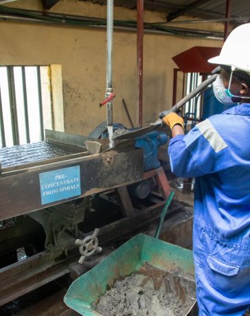 Trabalhador usando uniforme azul opera uma mesa vibratória para processamento de minério em uma unidade industrial.