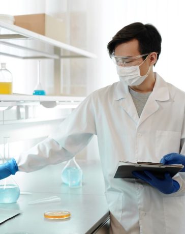 Dois pesquisadores usando jalecos analisam dados em um computador dentro de um laboratório.