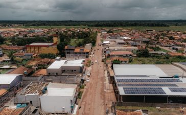 Vista aérea de uma comunidade amazônica com painéis solares instalados nos telhados, cercada por áreas verdes.