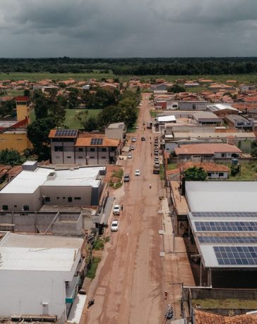 Vista aérea de uma comunidade amazônica com painéis solares instalados nos telhados, cercada por áreas verdes.