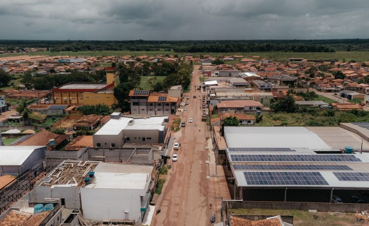 Vista aérea de uma comunidade amazônica com painéis solares instalados nos telhados, cercada por áreas verdes.