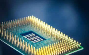 Close-up de um chip de computador com pinos dourados sobre fundo azul.