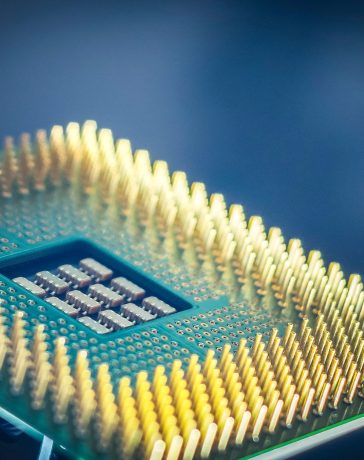 Close-up de um chip de computador com pinos dourados sobre fundo azul.