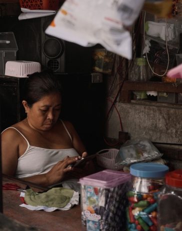 Mulher usa o celular dentro de um pequeno comércio repleto de produtos.