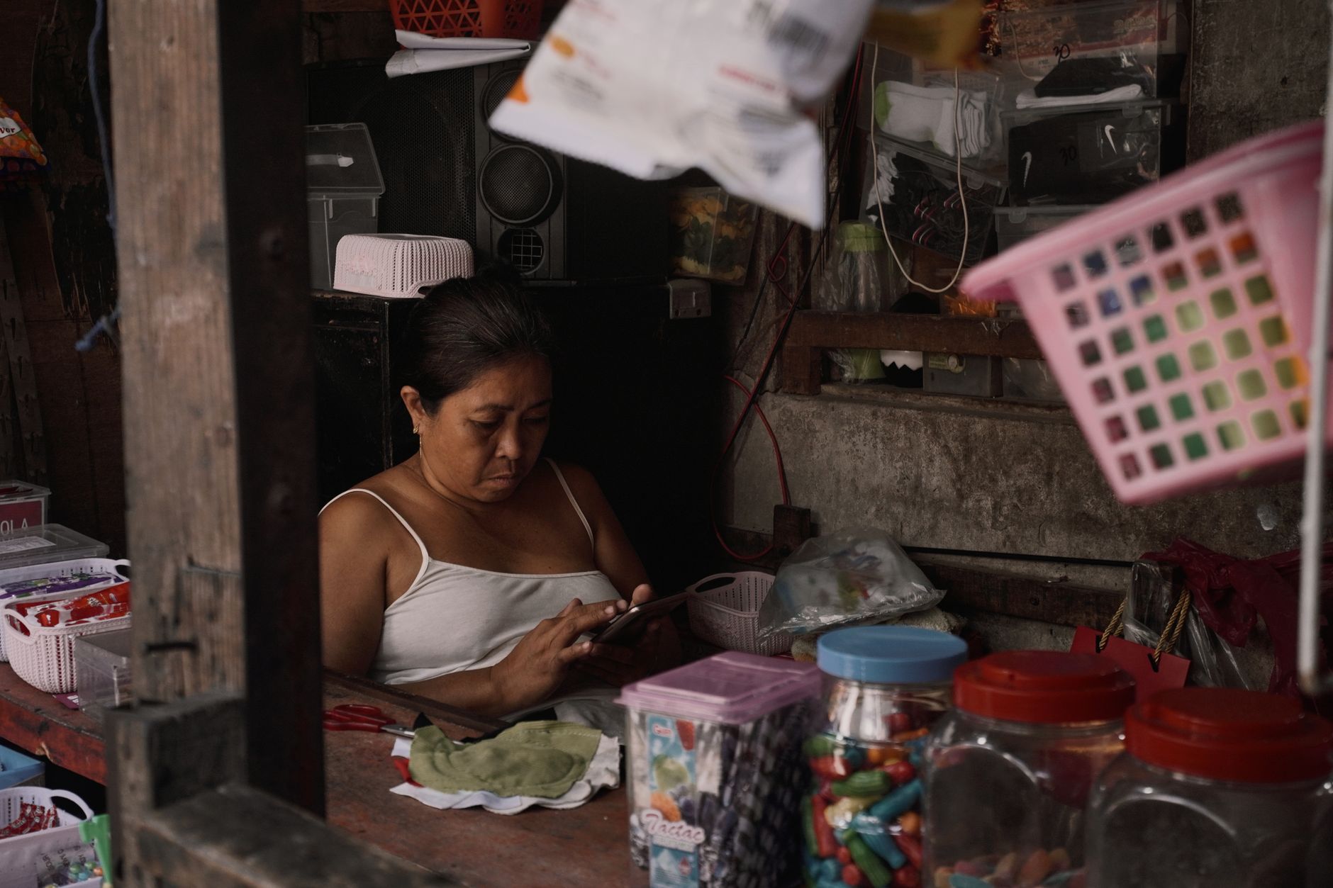 Mulher usa o celular dentro de um pequeno comércio repleto de produtos.