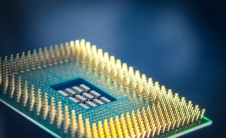 Close-up de um chip de computador com pinos dourados sobre fundo azul.